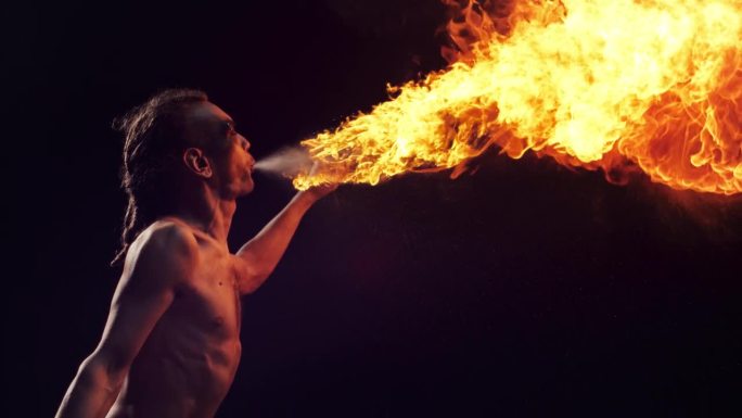 创意超级慢动作镜头。在嘉年华上，火焰表演者像龙一样喷出火焰。一个赤裸上身的男性火焰艺术家的肖像，正在