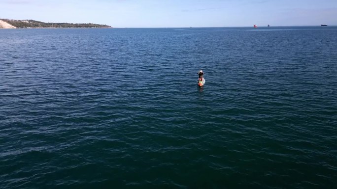 在开阔的海面上，一名男子在冲浪板上用信号镜发出求救信号