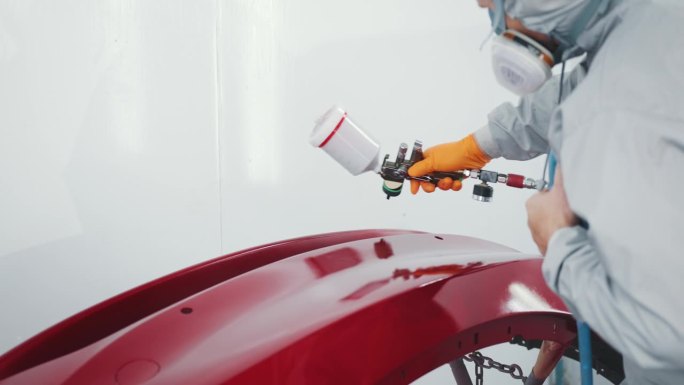 汽车喷漆工在专用展台车门上喷红漆。在汽车维修车间喷漆车辆零件。汽车制造厂。汽车涂料服务，优质汽车车身