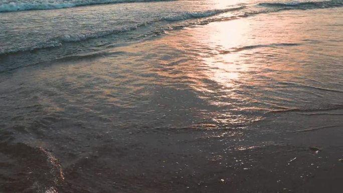 平静的海浪卷过沙滩。日落在海上或海洋。水的运动。海浪掀起阵阵泡沫。旅游的天堂。海滩旅游主题。太阳在波