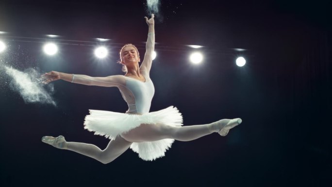 一位才华横溢的芭蕾舞演员在舞台上表演的肖像。年轻的女性在一个黑暗的工作室里做一个劈开跳跃和从她的手中
