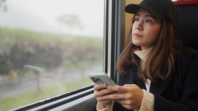 在火车上，漂亮的女游客坐在窗边用手机看窗外的风景