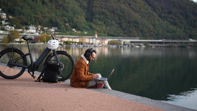 工作与自然相遇:一个人在湖边的木板路上骑着电动自行车和笔记本电脑