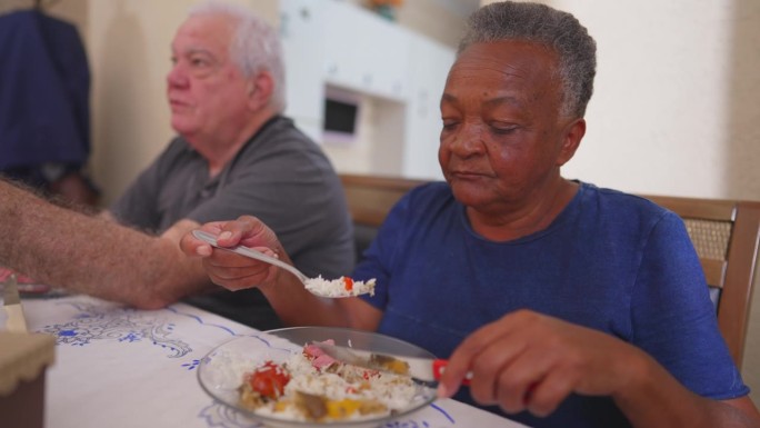 老妇人在吃午饭的时候，一群形形色色的老人过来吃饭。一位巴西老太太吃东西的特写