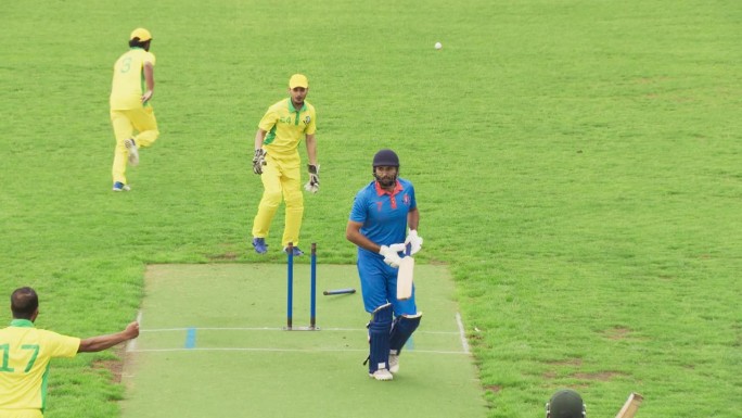 印度业余板球队在比赛前训练。蓝队击球手在三柱门被击碎后未能击中球而被投球出局。对手互相欢呼庆祝