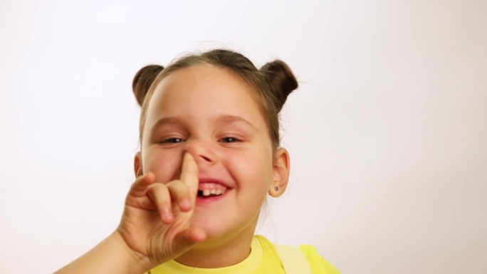 有趣的小女孩笑得很开心，因为牙齿掉了，嘴巴裂开了，抠着鼻子，特写，白色背景。快乐的无牙孩子。健康牙齿