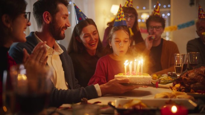 快乐微笑的女孩吹灭她美味的生日蛋糕上的蜡烛。年轻快乐的孩子被她的家人、亲戚和朋友包围着，坐在舒适的客