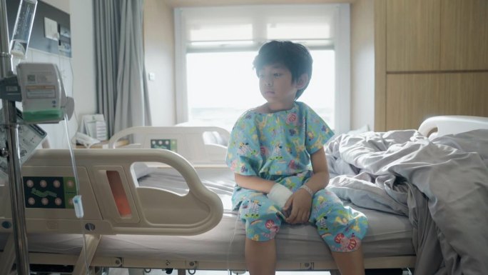 一个心烦意乱的男孩独自坐在医院的病床上，在医院里无聊地望着别处
