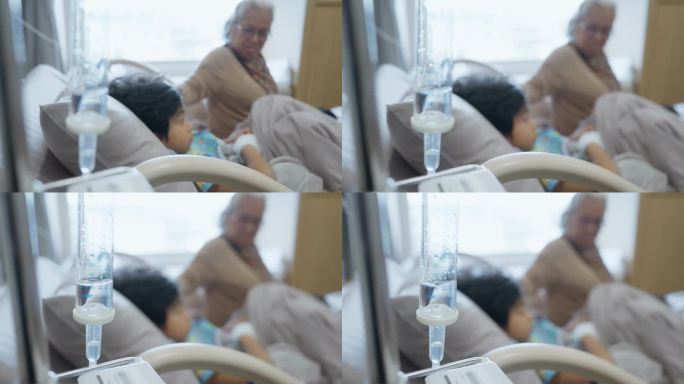 一位亚洲祖母抚摸着一个躺在医院病床上的小男孩的头，她表达了她的爱，并希望他早日康复。