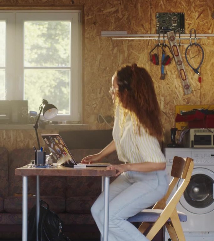 垂直屏幕:西班牙裔妇女打开车库门，坐在车库的笔记本电脑后面。女性电子商务创业公司创始人创建在线服务。