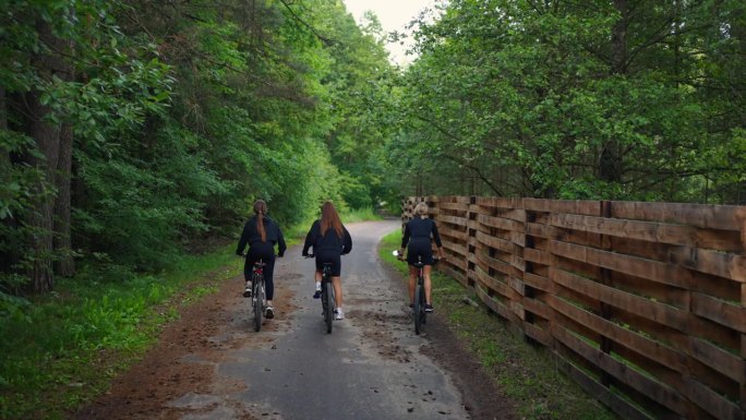 年轻苗条的妇女骑着自行车在乡村，在森林和木栅栏之间穿行