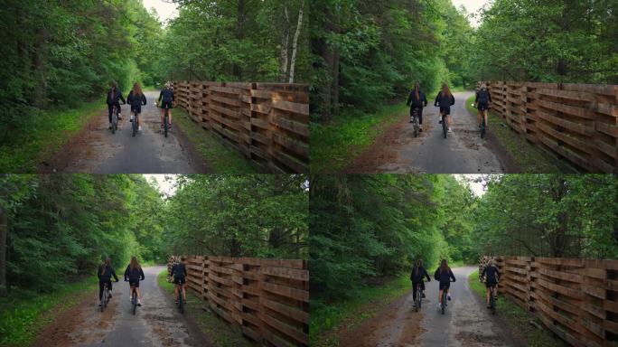 年轻苗条的妇女骑着自行车在乡村，在森林和木栅栏之间穿行