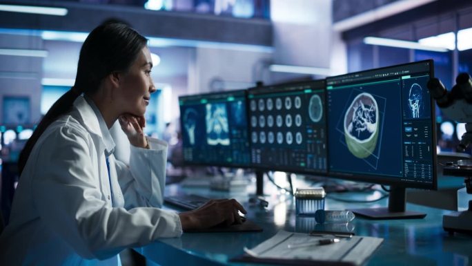 亚洲女性神经学家在现代医学研究中心实验室用台式电脑进行人脑CT扫描。专业医生在3D软件中观察病人的大