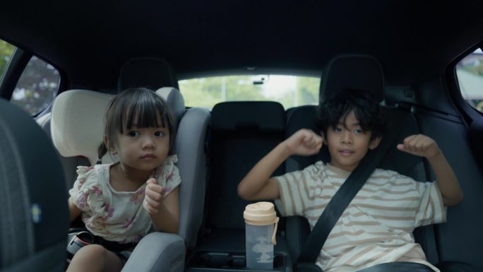 快乐的小男孩和妹妹在旅行时坐在汽车后座唱歌