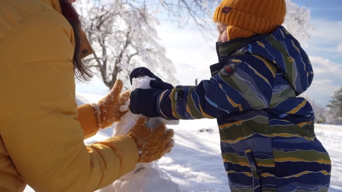 蹒跚学步的小男孩帮妈妈堆雪人