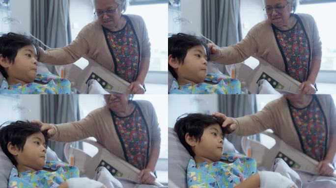 一位亚洲祖母抚摸着躺在病床上的小孩的头，她在病床旁表达她的爱。