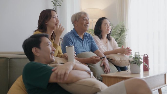 亚洲家庭在家里度过安静的夜晚。妈妈、女儿和爷爷坐在沙发上看电视。