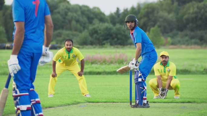 印度板球队在比赛前训练。蓝队击球手成功击球并冲刺得分。黄队急于接球