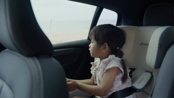 可爱的亚洲女孩坐在汽车座椅上，和家人一起开车旅行。