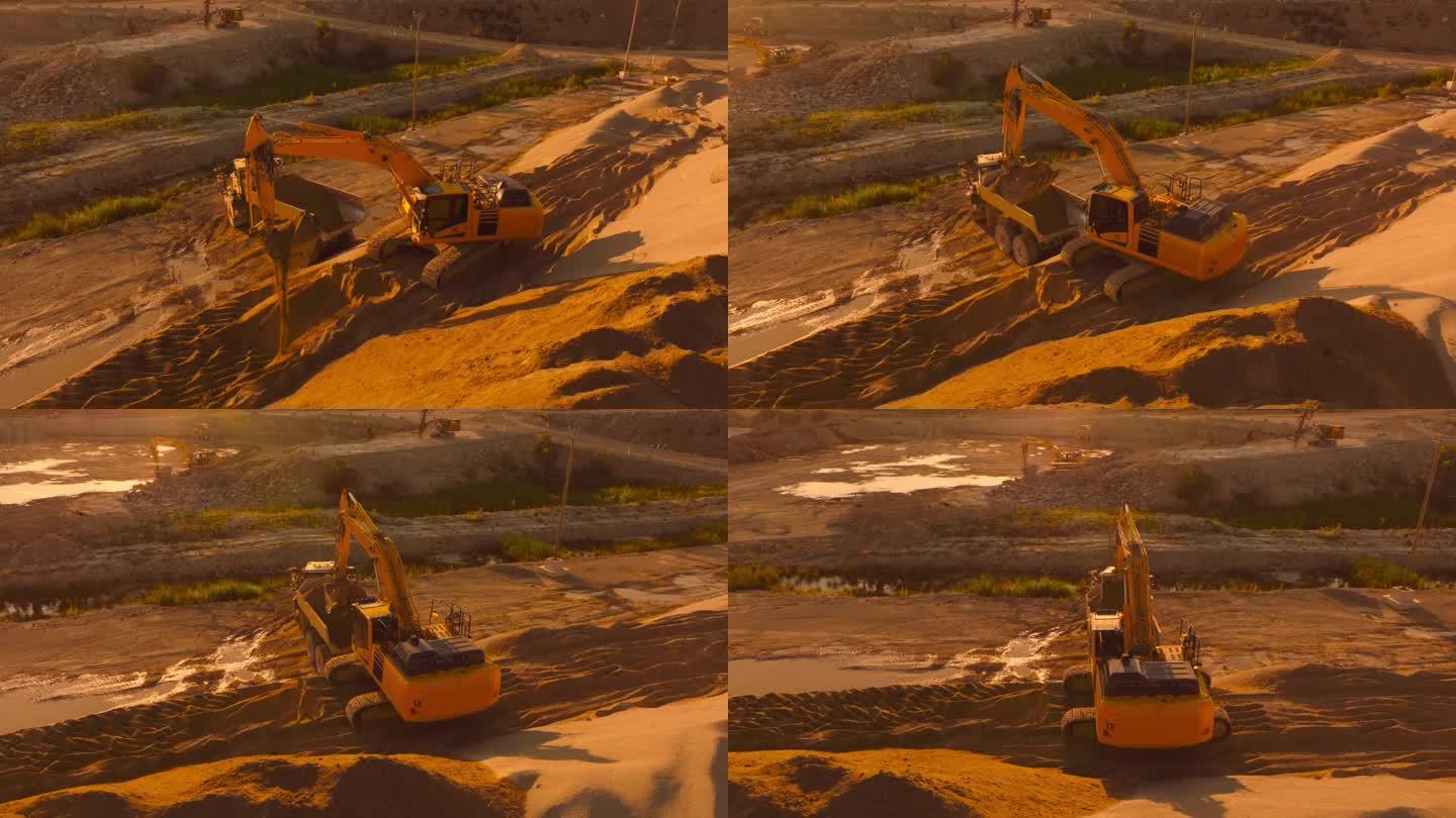 空中无人机拍摄的建筑工地在阳光明媚的晚上:工业挖掘机装载沙子到一辆卡车。建设新公寓楼的过程。操作重型