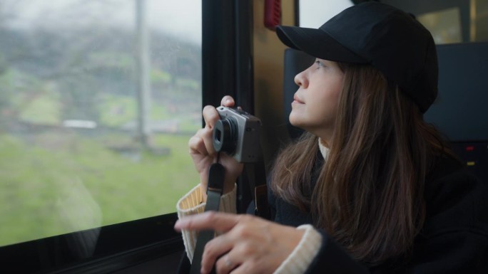 一名心情愉快的女子乘火车去瑞士山区度假时，从车窗拿起相机拍摄。