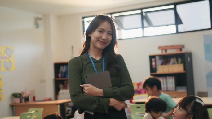 图为站在教室里对着镜头微笑的亚洲小学老师。