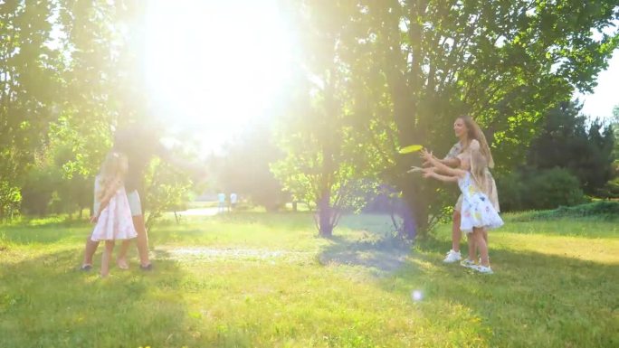 一家人在公园里扔飞盘。微笑的女孩抓飞盘。年轻的父母和女儿玩飞盘。享受夏日户外活动的家庭。真正的时间。