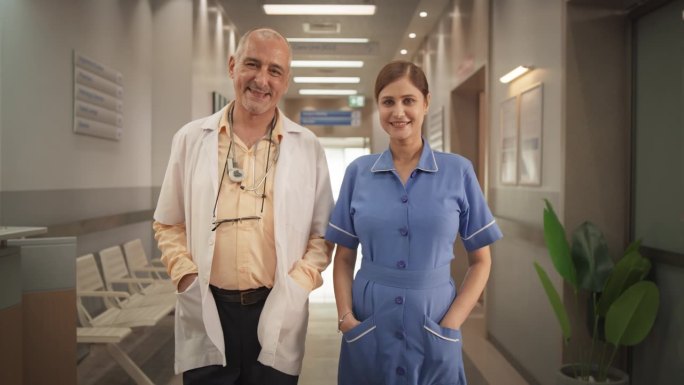 两位友好的印度医生和护士:一男一女成功的医疗保健专业人员站在现代医院办公室，摆姿势，看着镜头，微笑的