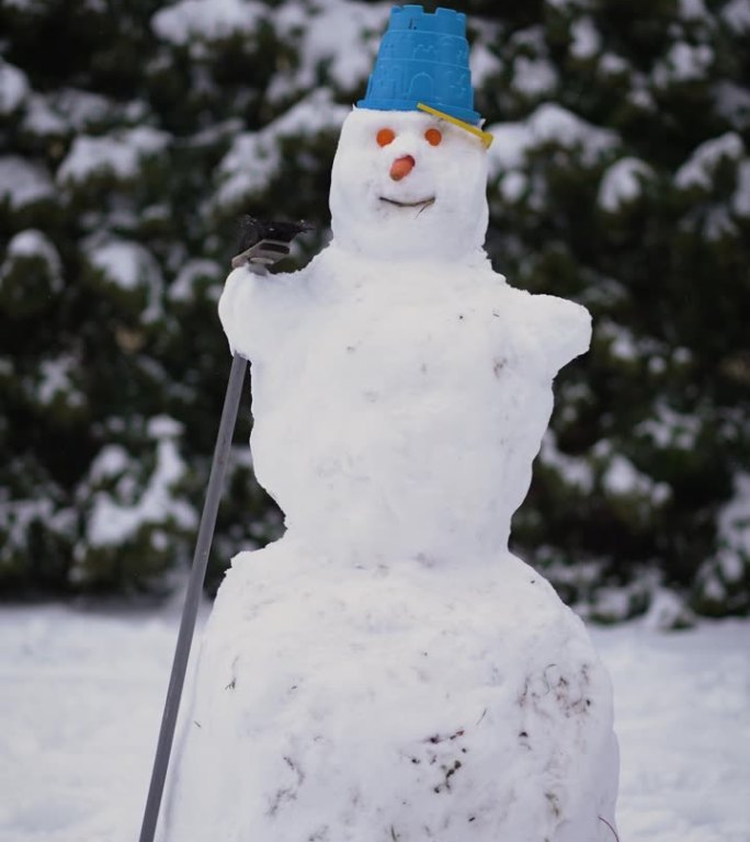 大雪人与胡萝卜的眼睛，鼻子，和斗帽栖息在它的头上在冬天和雪站在后院，垂直视频