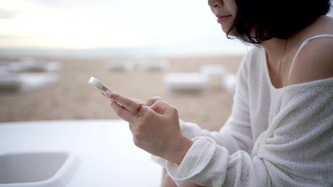 日出时在海边用手机发短信和滚动的女人的手特写。