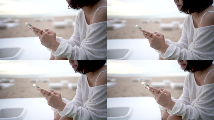 日出时在海边用手机发短信和滚动的女人的手特写。