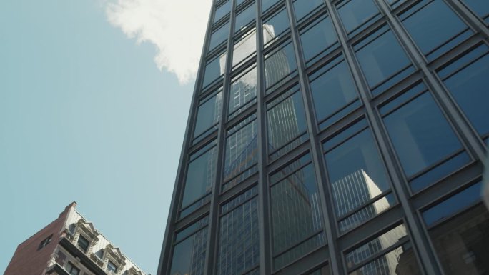 从现代玻璃建筑反射的商业摩天大楼的低角度镜头。在一个晴朗的晴天，从一辆移动的汽车上拍摄的纽约城市建筑