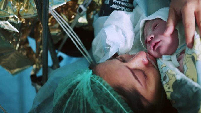医院里母亲抱着刚出生的婴儿。刚分娩的母亲把刚出生的婴儿抱在胸前。第一眼看到手术室里的妈妈和她的新生儿