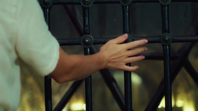 特写镜头中，女性的手触摸着金属栅栏格栅，女性的手指沿着格栅移动。