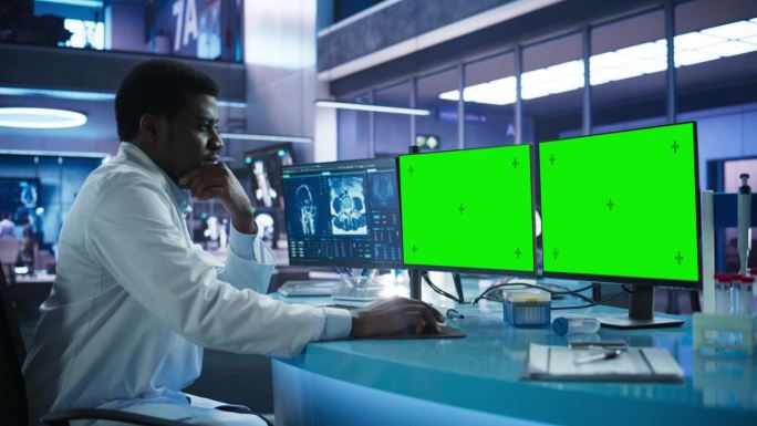 癌症研究中心医学实验室:黑人男性神经科学家使用桌面电脑与绿色屏幕铬色显示。专家研究脑肿瘤，寻找解决方