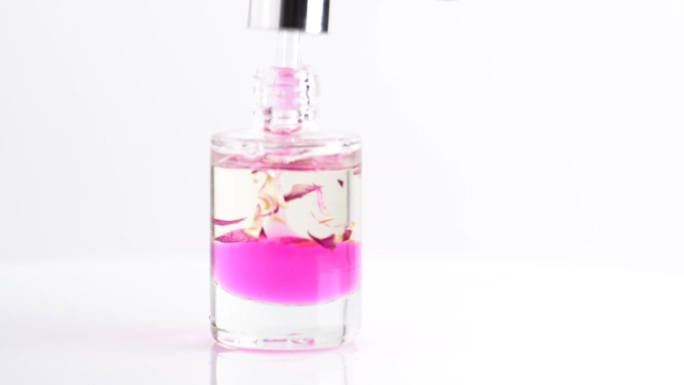 用移液器按摩化妆品粉色油，滴入透明的瓶子，特写。