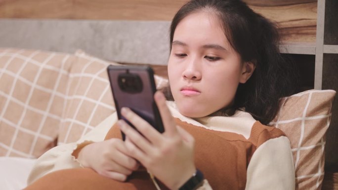 可爱的亚洲少女在睡觉前用智能手机躺在床上