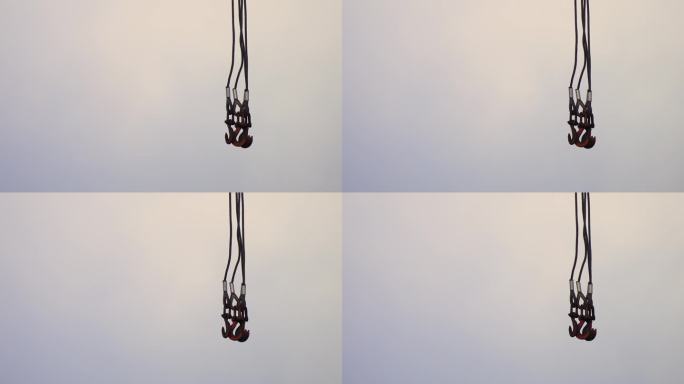 吊车的钢索带着金属钩悬挂在阴雨的灰色天空中，在风中摇摆。左侧用于放置文本的复制空间