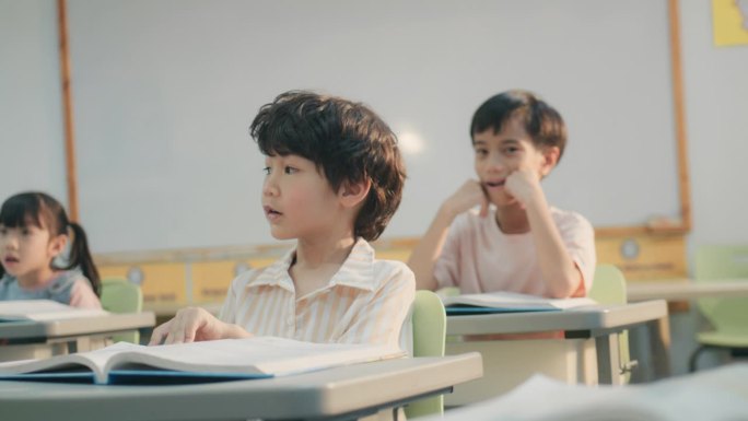 一个年轻的亚洲男孩在教室里专心地回答幼儿园老师的问题。