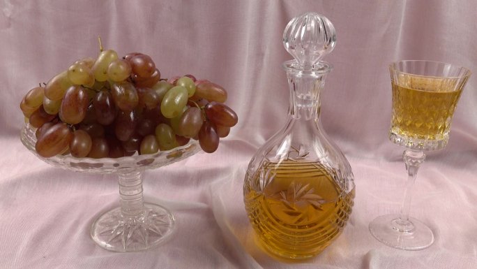 水晶花瓶与葡萄，水晶醒酒器和水晶饮用玻璃与白葡萄葡萄酒是在一个淡粉色缎面背景。