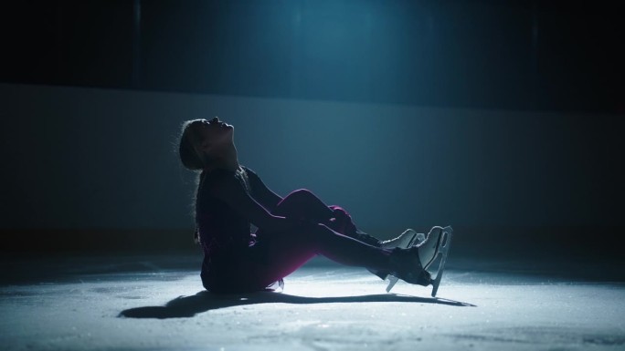 花样滑冰运动员十几岁的女孩坐在冰上，摔倒后哭泣，沮丧的女人的剪影