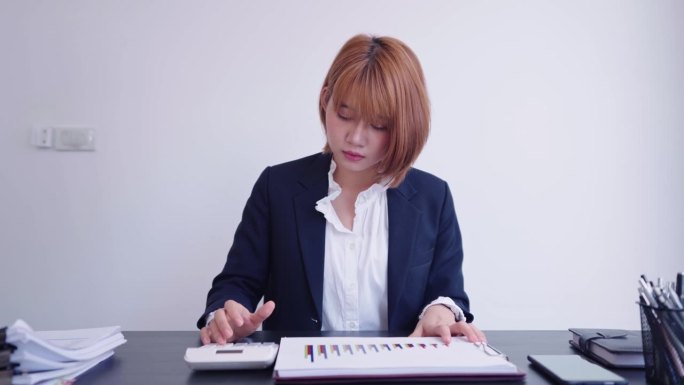 一位自信的亚洲女商人穿着职业装，在她的工作空间里勤奋地计算着公司的季度业绩。她专注于自己的任务。