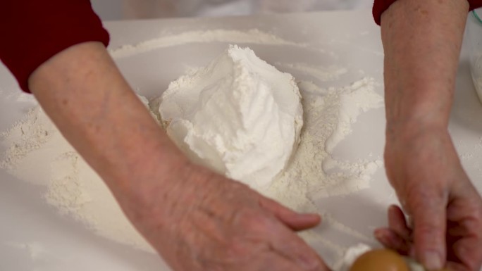 老妇人的手在厨房白色的桌子上移动新鲜的天然面粉。缓慢的运动。一步一步自制面团的准备