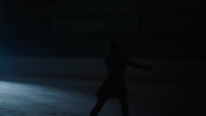 冰上移动女子的剪影，女子花样滑冰运动员在黑暗中滑行，慢动作