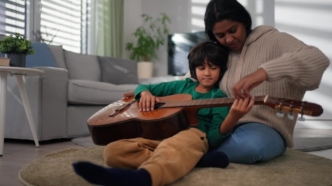 多种族的小男孩在家里和妈妈一起学弹吉他。