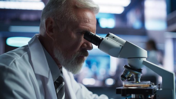 医学发展实验室:用显微镜近距离观察资深白人男性科学家，分析培养皿样品。制药实验室进行生物技术研究，开