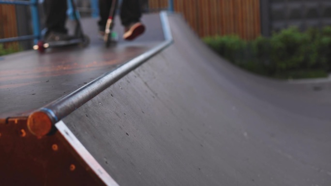 滑板公园里，孩子们骑着滑板车做着各种花样和特技，男孩们在滑板公园里骑着小轮自行车和滑板，在新的坡道上