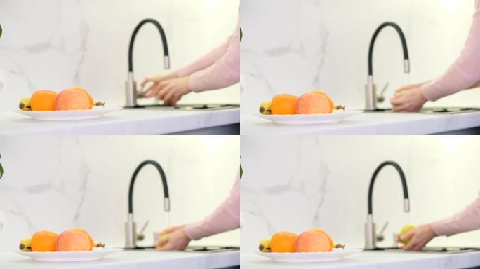 妇女在家厨房里洗水果和蔬菜。这个女孩用自来水洗水果。