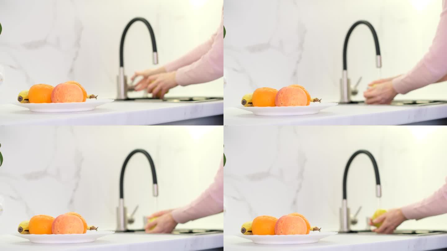 妇女在家厨房里洗水果和蔬菜。这个女孩用自来水洗水果。