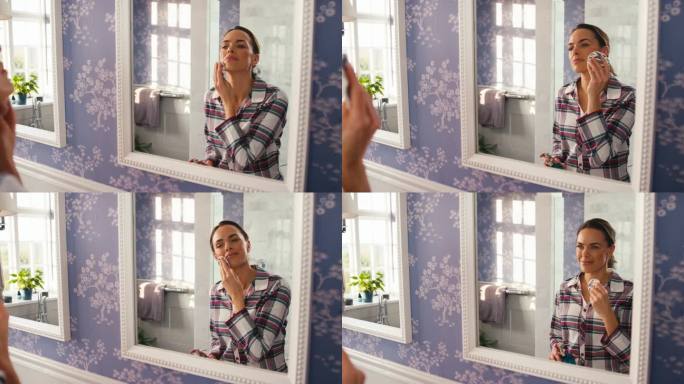 在家的女人在浴室镜子前用洗面奶和化妆垫卸妆